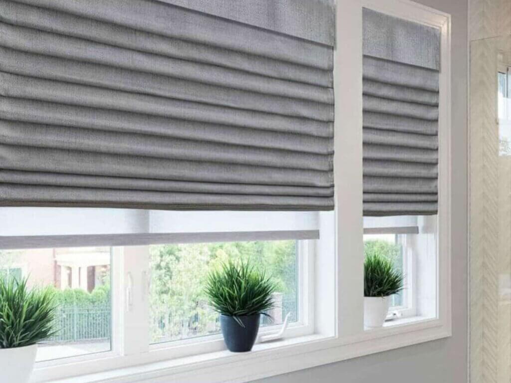 gray roman shades hanging on a window, partially raised, showcasing their elegant and classic fabric folds.